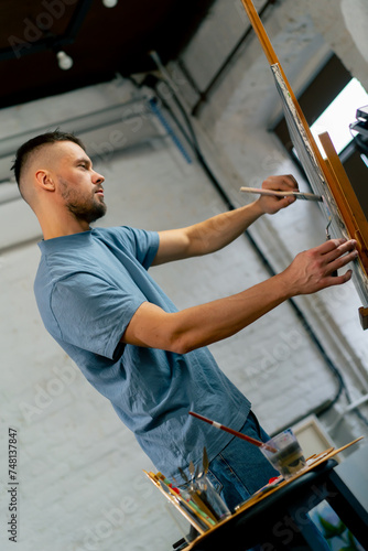 in an art workshop an artist in a blue T-shirt makes broad strokes on the canvas with wide and flat brush
