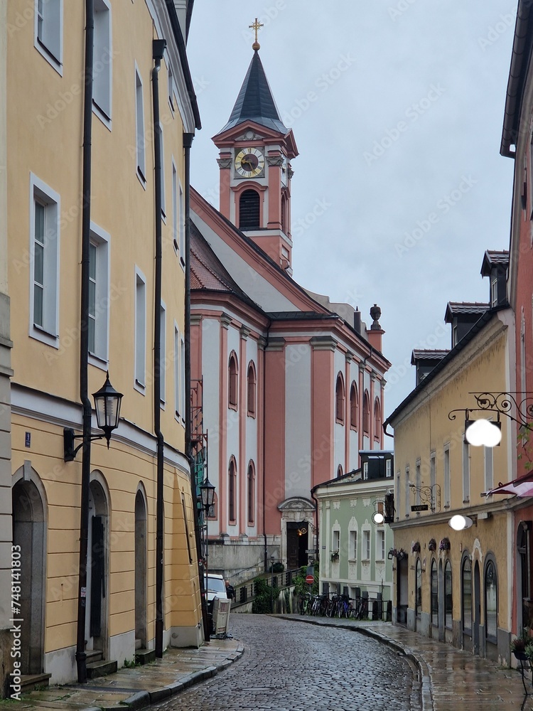 Old Centar city of Passau, old paved street during rainy day in Bavaria, Germany. Cobblestone streets in Passau.Parish church St. Paul in the old town of Passau.