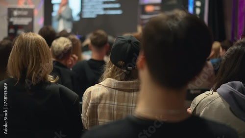 Panning audience of people at seminar in conference room. Young adults men and women sit in loft-style venue, embodying vibrant startup ecosystem and entrepreneurial spirit