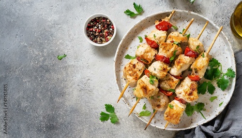Chicken kebab skewers on a plate over light yellow slate, stone or concrete background. 