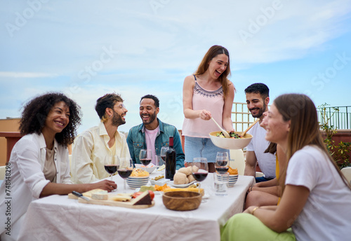 Canvas Print A group of people is gathered around a table, sharing food and wine while smiling and enjoying the leisurely event