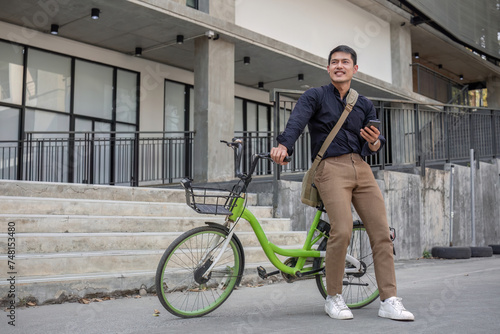 A young Asian businessman rides a bicycle to work. Standing outside the office talking on the phone and talking about business. Concept of reducing energy and reducing air pollution.