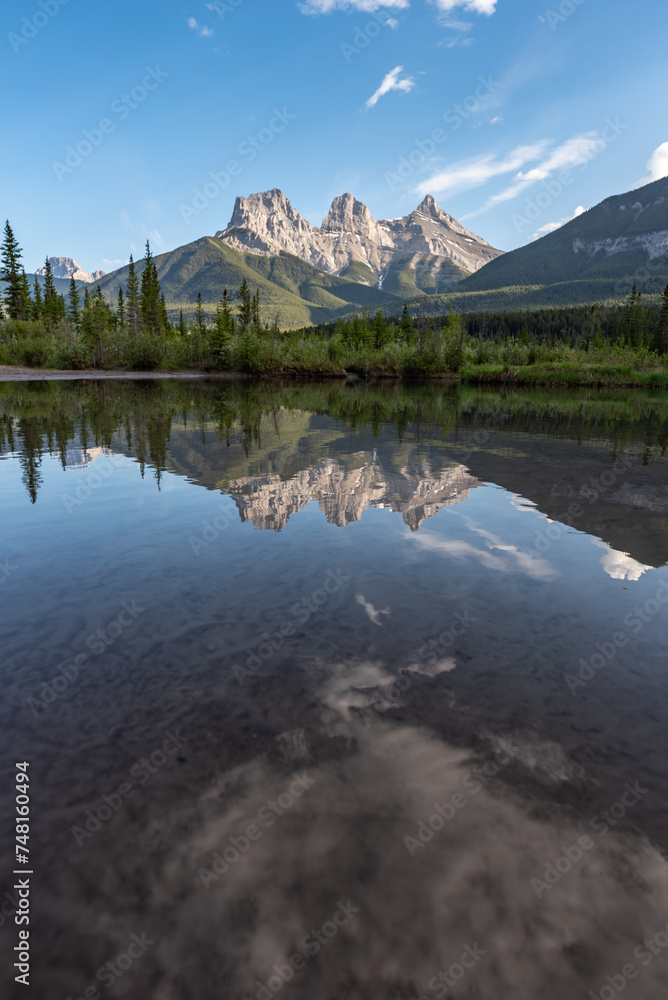 Incredible view of Three Sisters in Canada, Banff National Park with mountains reflecting in calm, lake, water below blue sky, pristine, perfect wilderness setting. 
