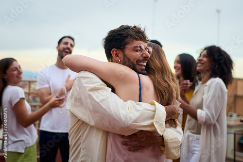 A group of people is joyfully embracing greet each other in a gesture of happiness and unity at a lively party. Together they are sharing a moment of fun and entertainment. Concept of friendship © CarlosBarquero