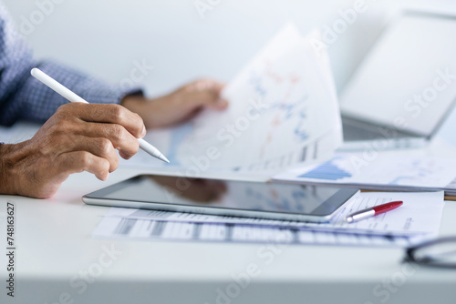 Businessman in office using tablet with documents and chart for analyzing data of investment to make investment plan for a future, financial investment concept.