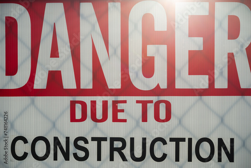 Danger Due To Construction sign tied to a chainlink fence with sun backlight photo