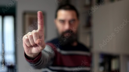 Bearded man standing with serious expression saying no with finger at home.
