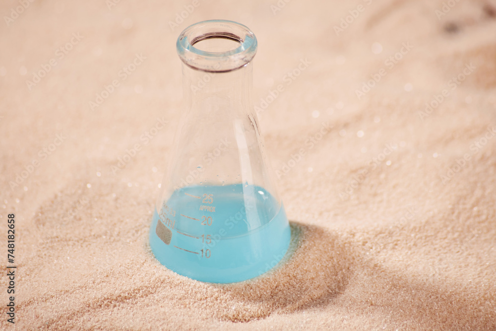 Pure clean glass chemical cone flask with bright blue liquid inside on the clean sand surface background Pure clean glass chemical cone flask with bright blue liquid inside on the clean sand surface background