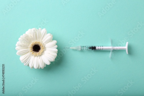 Cosmetology. Medical syringe and gerbera flower on turquoise background, flat lay photo