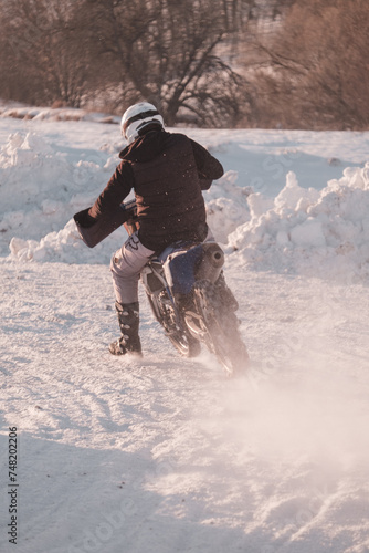 Racer on a motorcycle rides in turn of wheels a spray of snow and mud. Skid on a snowy road. The snow from under the wheels of a motorcycle Enduro.