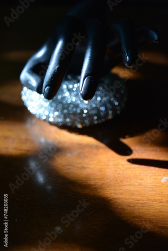 Black statuette of a matte female hand with a metal sponge on a brown wooden table of the old style with the sun rays.