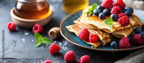 A plate holds a stack of fluffy pancakes, topped with a vibrant assortment of fresh berries and garnished with sprigs of mint. The colorful toppings contrast beautifully with the golden pancakes