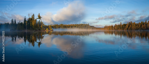 Panorama of blue lake in northern Minnesota with an island and pines on a foggy September morning