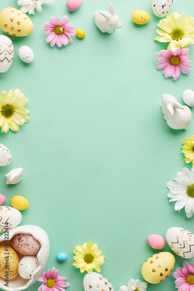 Easter celebration: spring's vibrant embrace. Top view vertical shot of easter eggs, white and pink daisies, bunny figurines and sugar sprinkles on teal background with space for warm wishes
