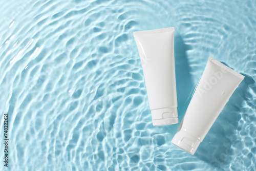 Natural beauty: embracing organic cosmetics. Top view shot of two white skincare tubes floating on a serene blue water background, offering ample space for promotional content