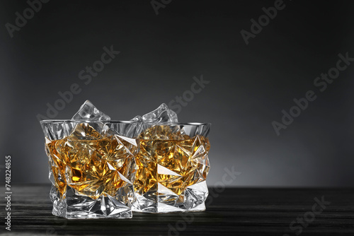 Whiskey and ice cubes in glasses on black wooden table, closeup. Space for text