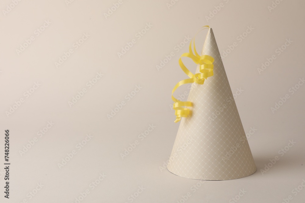 One beautiful party hat with serpentine streamer on beige background. Space for text One beautiful party hat with serpentine streamer on beige background. Space for text