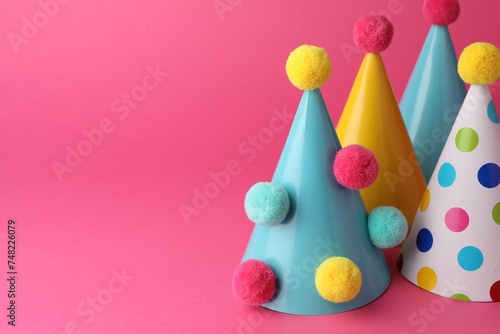 Beautiful party hats with pompoms on pink background, space for text