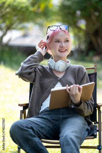 Young Happy Asian artist woman drawing book and wearing headphone, the artist paints in the garden © Wuttichaik