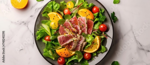 A plate of food featuring tuna tataki salad with lettuce, tomatoes, and oranges, elegantly presented on a marble table. The dish showcases a colorful blend of fresh ingredients.
