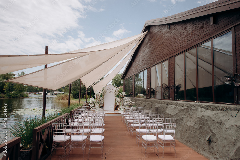 Obraz premium chiavari chairs. Outdoor wedding ceremony. wedding arch decorated with fresh white flowers with transparent chairs standing in the garden. Day of celebration, transparent chairs for guests