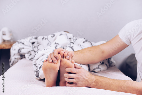 Bare feet of a child. The child is sleeping in bed. Legs look from under the blankets. Legs and heel. Hands tickle photo