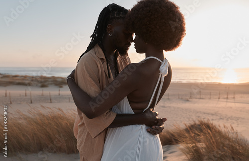Happy black couple standing and embracing on sand with dry grass plants