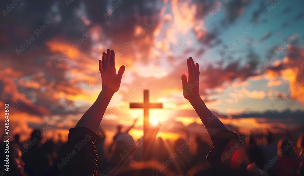hands raised up to a cross with sunset background