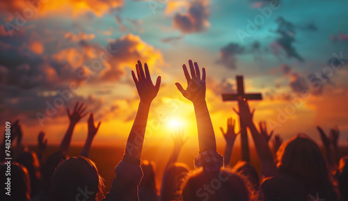hands raised up to a cross with sunset background photo