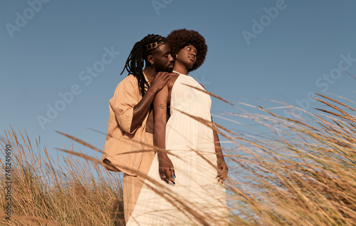 Happy black couple standing cuddling near dry grass plants in daylight