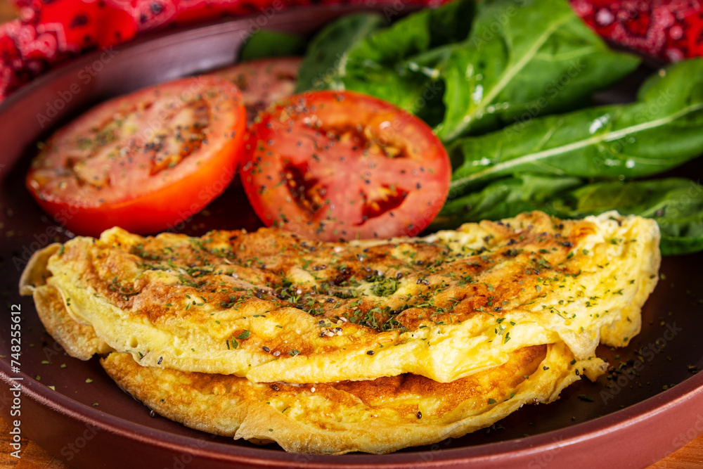 plate with an omelet and salad of sliced tomatoes and arugula