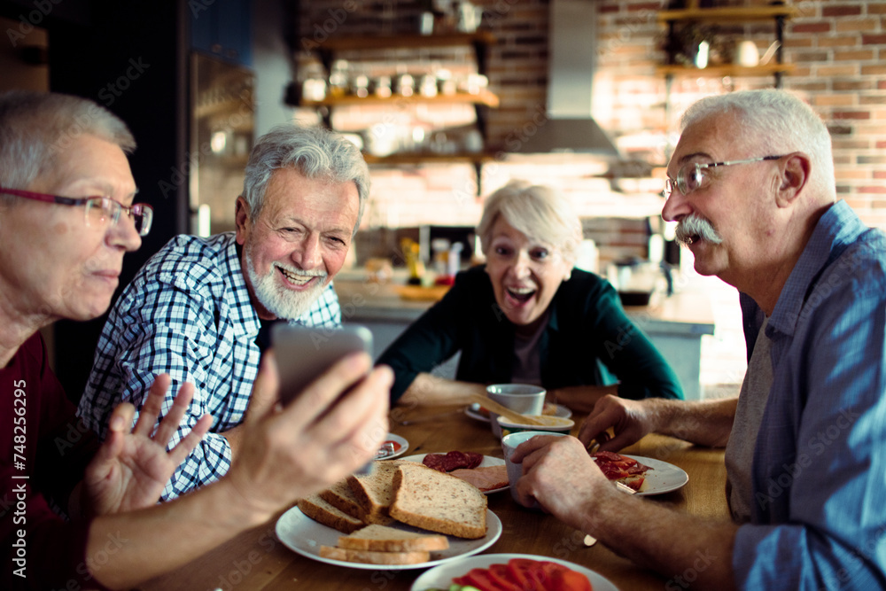 Senior friends laughing and sharing photos on smartphone at breakfast Senior friends laughing and sharing photos on smartphone at breakfast