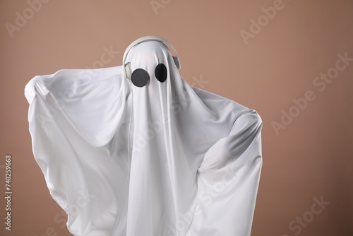 Person in ghost costume with headphones on dark beige background, space for text