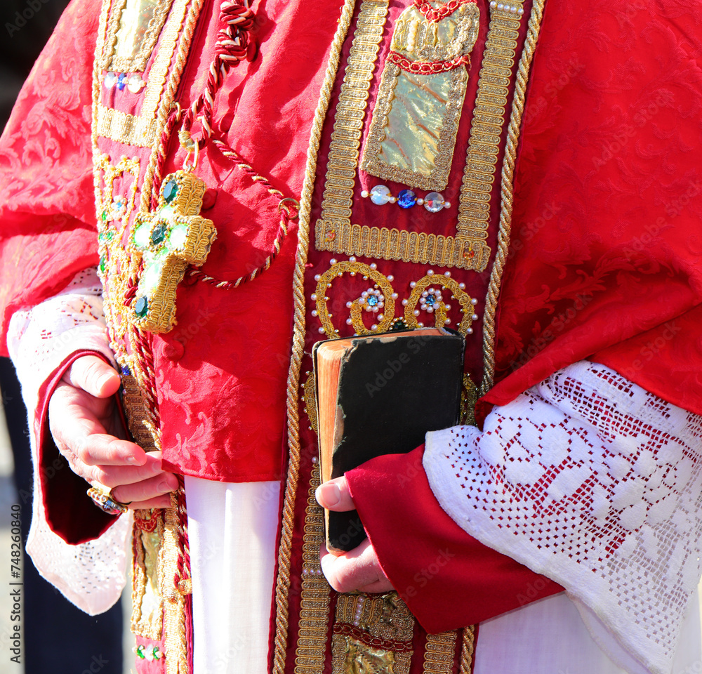 bible with in the hands of the bishop during the religious rite with red clerical dress