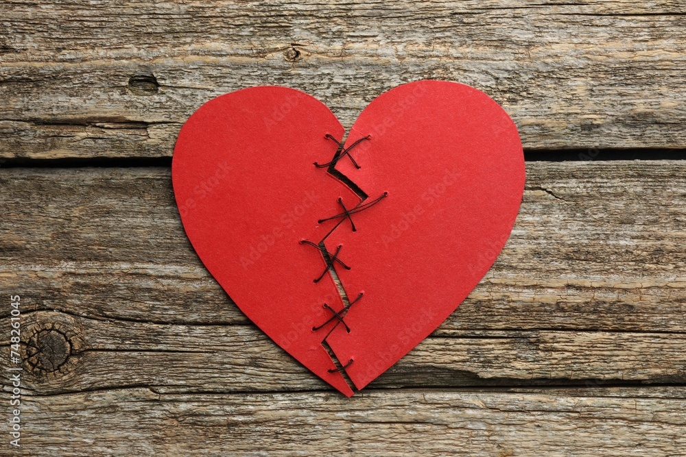 Broken heart. Torn red paper heart sewed with thread on wooden table, top view Broken heart. Torn red paper heart sewed with thread on wooden table, top view