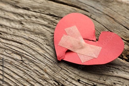 Fototapeta Naklejka Na Ścianę i Meble -  Broken heart. Torn red paper heart with medical adhesive bandages on wooden table, closeup with space for text