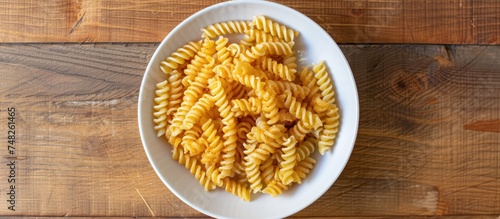 A birds eye view of fusilli pasta served in a white bowl placed on a wooden table, under the illumination of natural light.