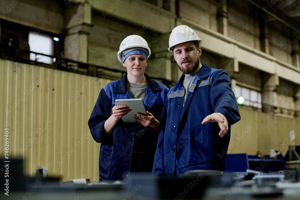 Medium shot of male and female colleagues working in plant warehouse discussing problems Medium shot of male and female colleagues working in plant warehouse discussing problems