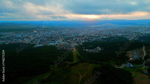 Fototapeta Naklejka Na Ścianę i Meble -  Aerial of the city and big green hills. Clip. Summer big city and cloudy sky during sunset.