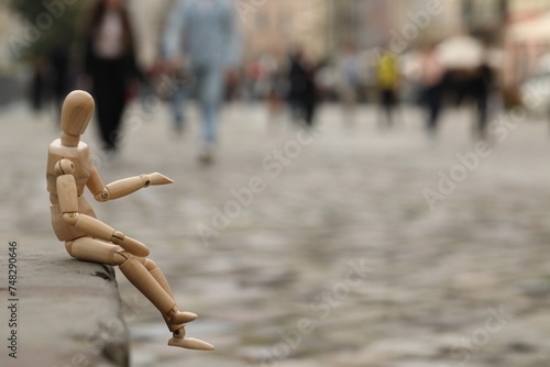 Wooden human figure sitting on curb outdoors, space for text