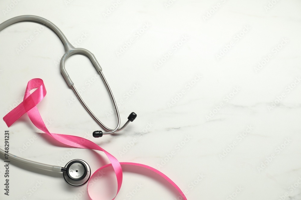 Fototapeta premium Breast cancer awareness. Pink ribbon and stethoscope on white marble table, flat lay. Space for text