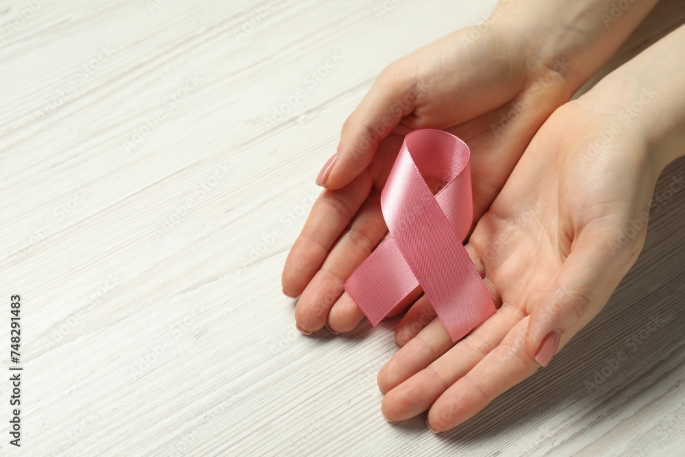 Breast cancer awareness. Woman with pink ribbon at white wooden table, closeup. Space for text Breast cancer awareness. Woman with pink ribbon at white wooden table, closeup. Space for text
