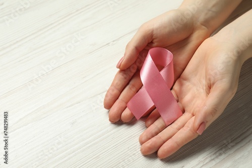 Breast cancer awareness. Woman with pink ribbon at white wooden table  closeup. Space for text