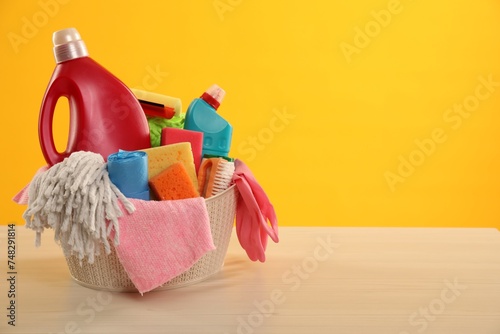 Different cleaning products in basket on wooden table against yellow background, space for text