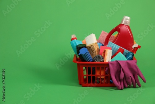 Different cleaning products in plastic basket on green background, space for text