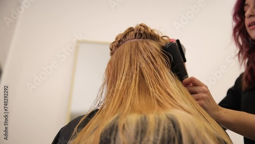 A woman is having her layered hair straightened by a hairdresser photo
