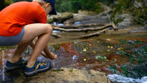 Tourist boy puts his hands in the river to drink cold clear water. Creative. Young boy drinking water from spring.