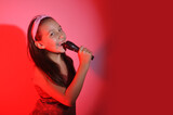 menina pré adolescente cantando com microfone em karaoke, fundo vermelho 