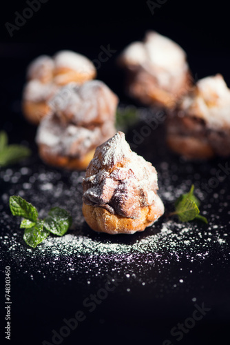 Profiteroles or cream puff with filling,  falling powder sugar topping. Berries, mint on black background. Fresh homemade Cream Puffs, cake, tasty French choux puff, ecler, dessert closeup. Vertical  © Subbotina Anna