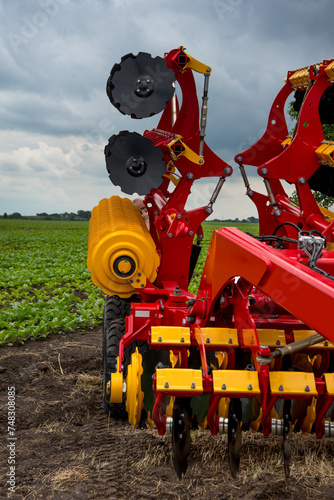 red and yellow harrow-cultivator standing folded for transportation near a field